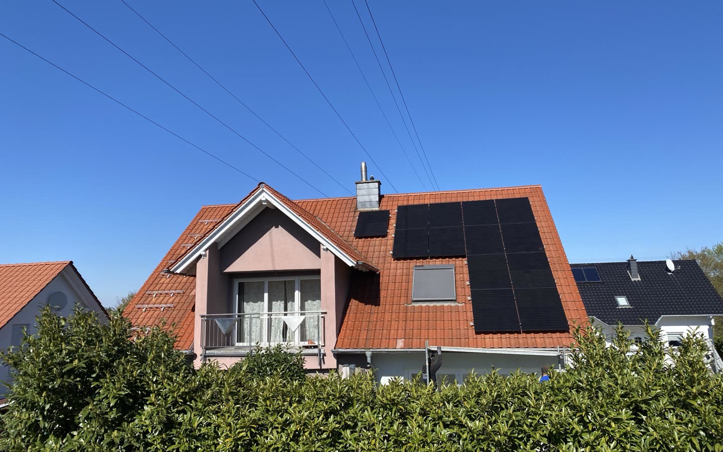 Einfamilienhaus mit rotem Ziegeldach und schwarzen Photovoltaikmodulen neben dem Kamin